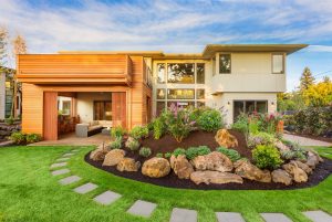 Modern two-story home with wood and white paneling, featuring a landscaped garden with vibrant flowers, stepping stones leading to the entrance, and meticulous lawn care services for an impeccably maintained look.