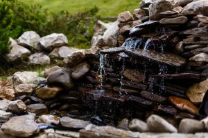 Tranquil garden oasis featuring a small, artfully arranged stone waterfall at Talking Rock Golf Club, gently cascading into a serene pond below.