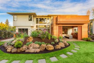 Modern suburban home with a mix of wood and white exterior finishes, featuring a beautifully landscaped garden by Landscape Design Prescott with flowers, shrubs, and stepping stones leading to a welcoming entrance at golden hour