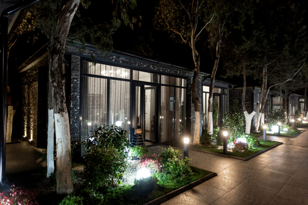Modern glass building illuminated at night with outdoor lighting, nestled among trees and lit pathways in a serene Prescott setting.