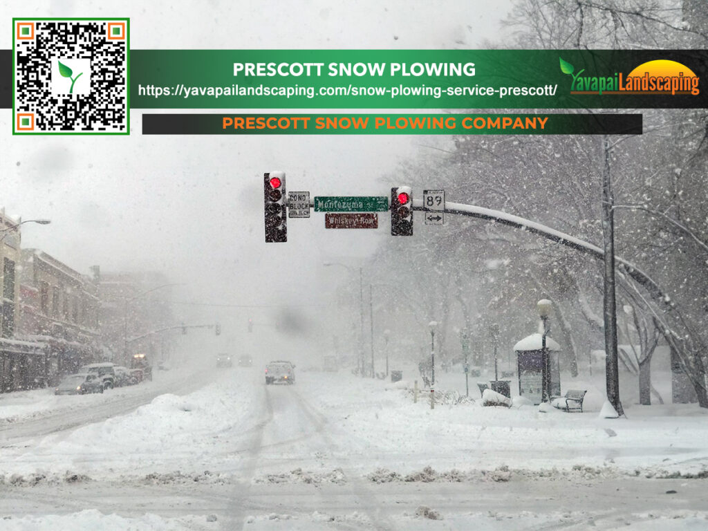 A snowy street during a heavy snowfall with a traffic light and a banner advertising "prescott snow plowing" with a web address and a qr code for yavapai landscaping.