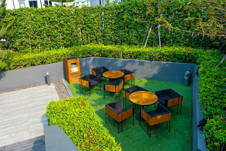 A modern outdoor lounge area with stylish wooden furniture, lush greenery, and neatly trimmed hedges providing a tranquil urban oasis, featuring 10 stunning landscape design ideas.