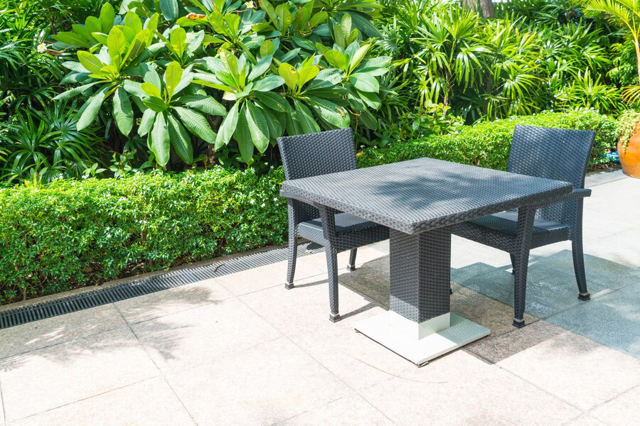 A tranquil outdoor patio setup featuring a modern black woven table and two matching chairs against a lush backdrop of vibrant green foliage, embodying principles of eco-friendly landscape design.