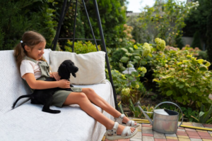 A young girl enjoys a serene moment with her black puppy on a garden bench, surrounded by lush greenery in an eco-friendly landscape design.
