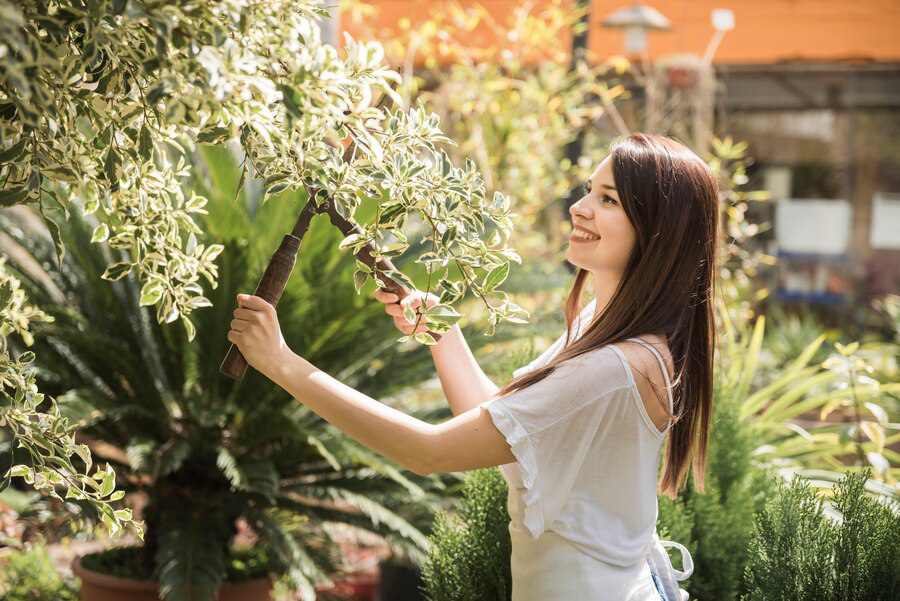 A young woman with a cheerful smile pruning a plant in a sunlit garden.