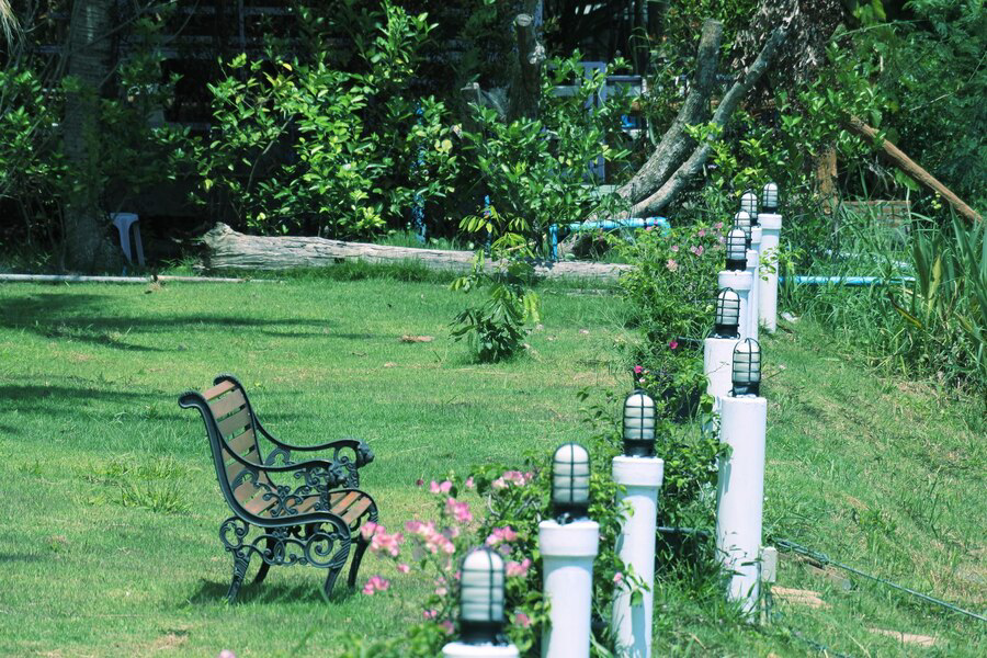 Tranquil garden scene with Prescott Landscaping Ideas for a vintage bench beside a neatly trimmed lawn, lined with white posts and flowering plants, inviting relaxation amidst greenery.