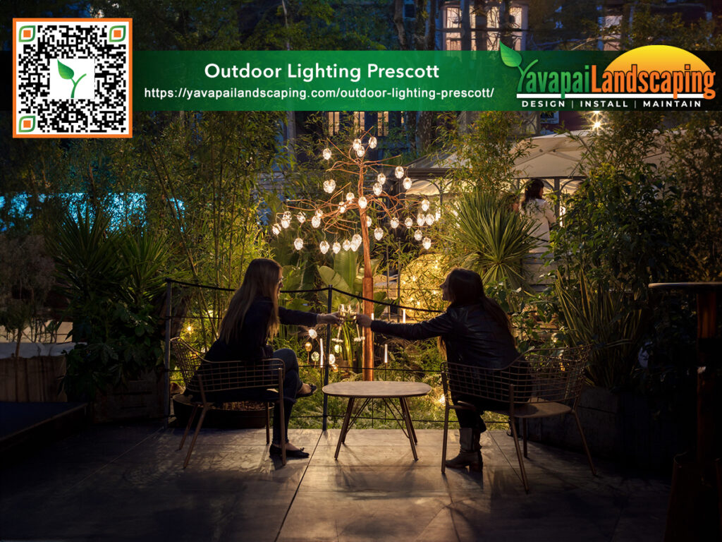 Two individuals enjoying an evening outdoors, sitting at a cozy patio table surrounded by lush greenery and illuminated by a warm glow from decorative lights.