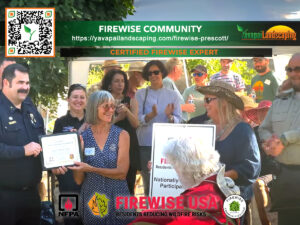 Group of people, including a firefighter, smiles and claps as two women in the center receive certificates at a firewise community event outdoors.