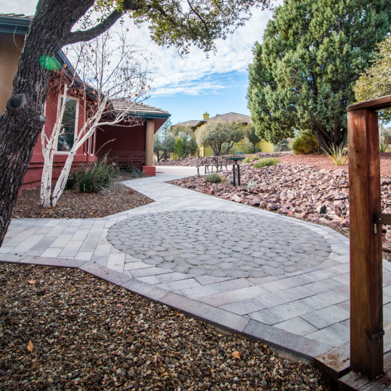 A brick walkway leads to a charming house surrounded by lush trees, resembling a picturesque gallery in an artist&#039;s portfolio.