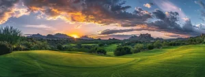 a lush green golf course with a vibrant sunset casting a warm glow over the rolling hills and trees, highlighting the beauty and serenity of the talking rock prescott golf club.