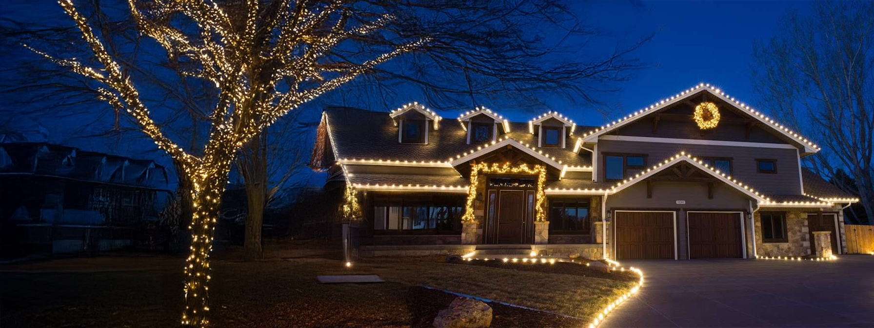 A premier house in Prescott showcases a stunning Christmas light installation, with white lights elegantly outlining the roof and windows. The front yard tree is also wrapped in lights, casting a festive glow against the dark evening sky.