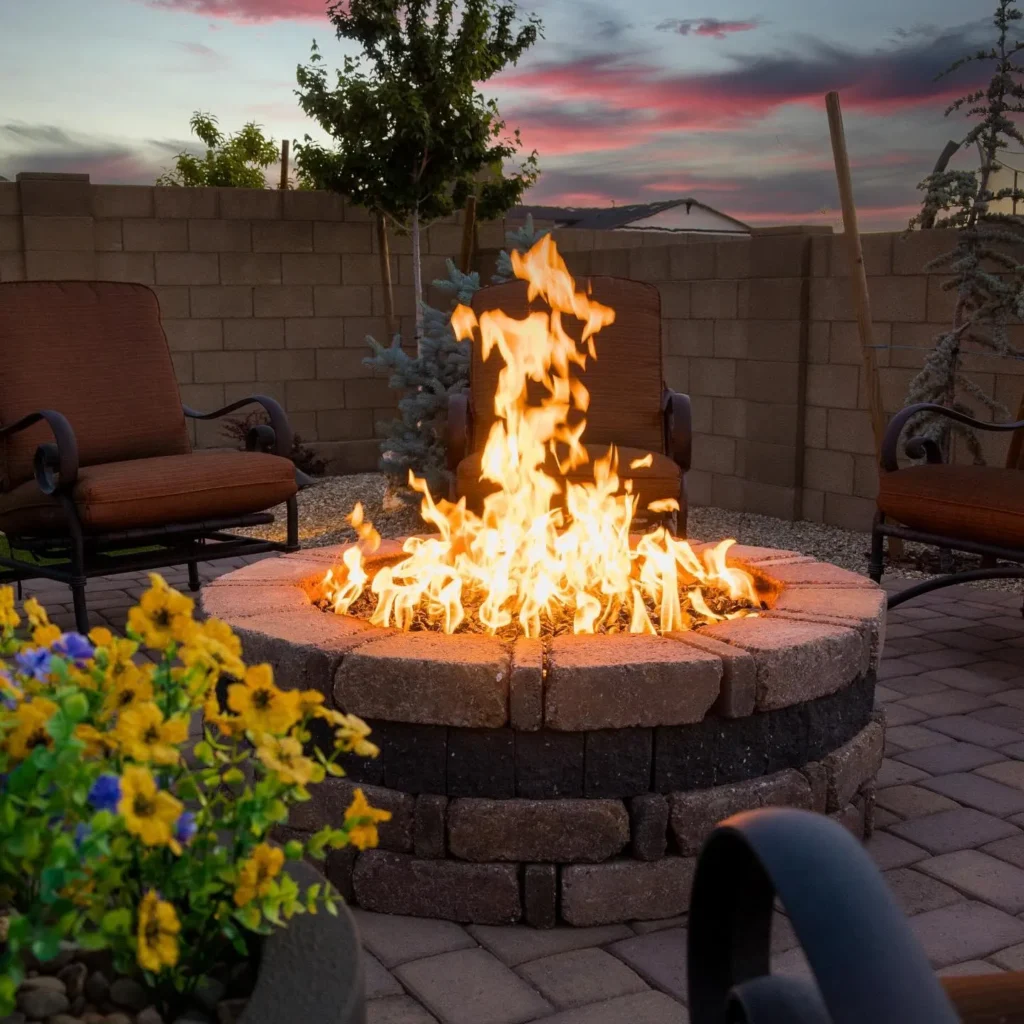 Fire pit surrounded by two chairs, colorful flowers, and a sunset sky, showcasing an inviting outdoor space designed by Yavapai Landscaping.