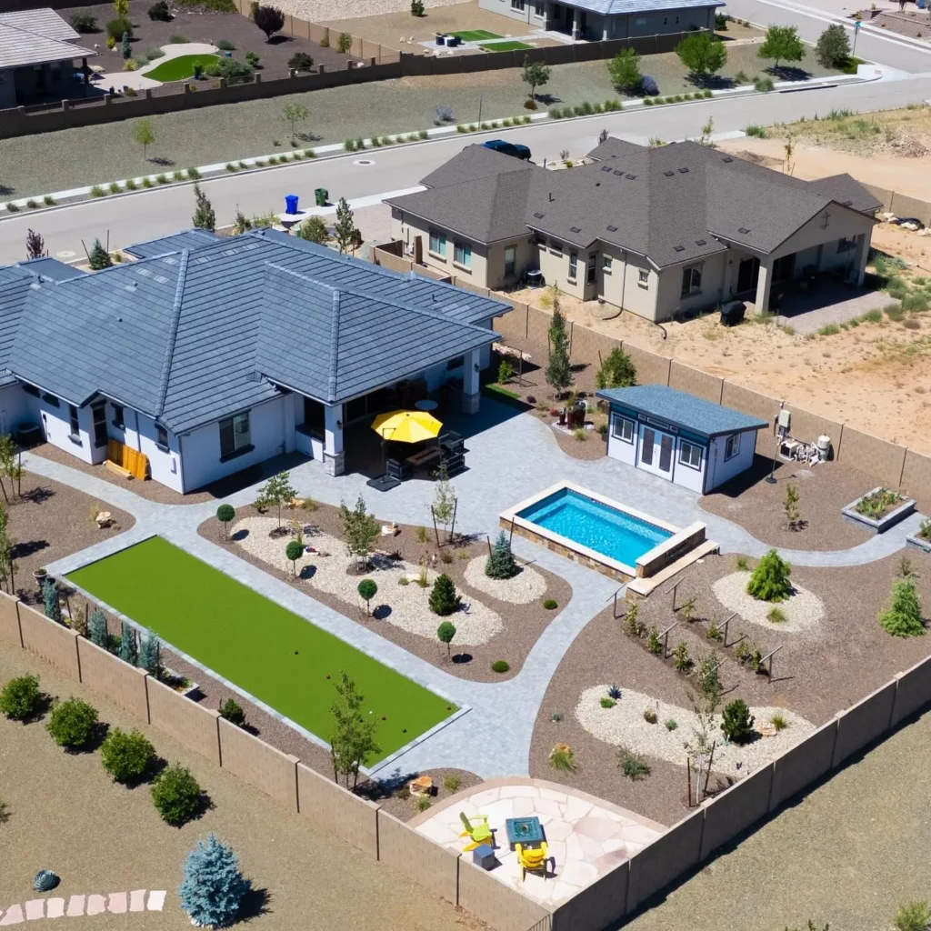Aerial view of a modern home with landscaped yard featuring a swimming pool, patio seating area, artificial turf, and decorative trees, showcasing Yavapai Landscaping's quality outdoor design and craftsmanship.