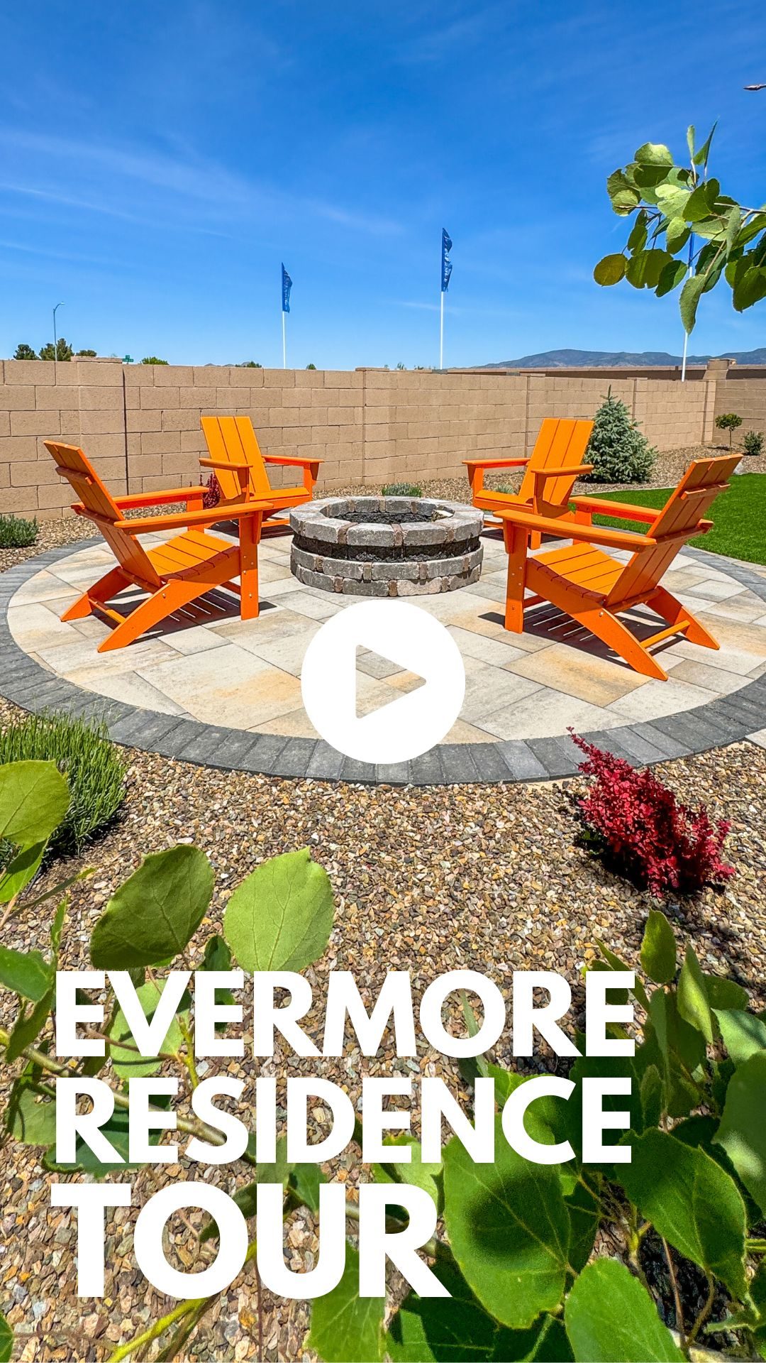 A sunny backyard scene featuring a circular stone fire pit surrounded by four bright orange Adirondack chairs on a stone patio. Blue flags wave in the background, with the text "RADIL RESIDENCE TOUR" at the bottom over gravel and greenery.