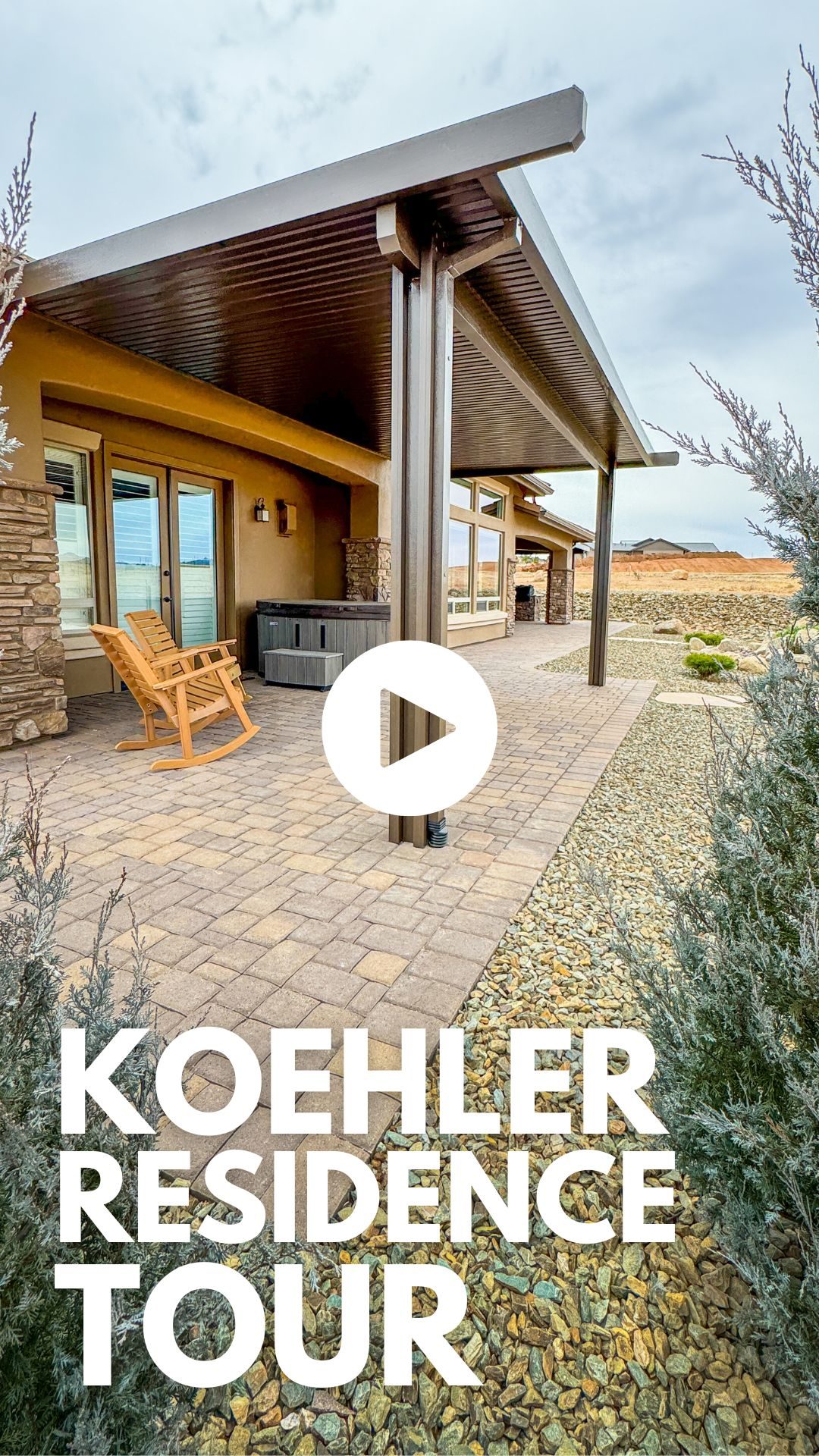 Image of a modern patio with a wooden rocking chair and hot tub placed under a covered structure. The patio is surrounded by a landscaped garden with gravel and greenery. Text reads "Koehler Residence Tour." A play button is overlaid in the center.