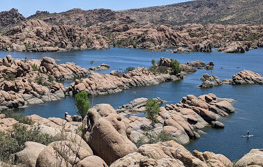 Scenic view of Watson Lake surrounded by granite boulders and greenery, featuring people kayaking and enjoying the natural landscape, highlighting outdoor recreational opportunities in Prescott, Arizona.